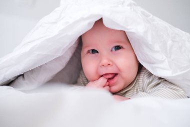 Yatak odasında beyaz battaniyenin altında gülümseyen sevimli bir oğlan. Yeni doğmuş çocuk yatakta dinleniyor. Aile sabahı evde. Yeni doğmuş bebekler.