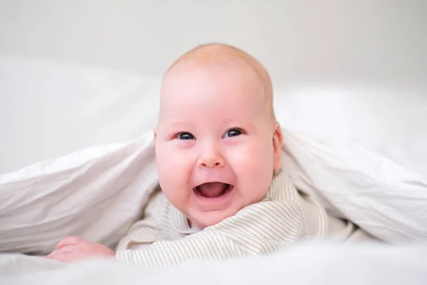 Schattige lachende kleine jongen onder een witte deken in de slaapkamer. Pasgeboren kind ontspannen in bed. Familie ochtend thuis. Pasgeboren zuigelingen — Stockfoto