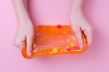 Yanlara renkli turuncu balçık geren bir çocuk. Çocuk elleri pembe arka planda sümüklü oyuncak oynuyor. Balçık yapıyorum.