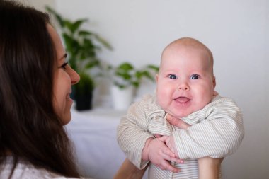 Mutlu bebek. Küçük sevimli tombul beyaz beyaz bebek anne ellerinde kameraya bakıp gülümsüyor. Aile hayatı, anneler sevgisi, annelik.