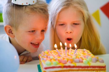İki sarışın beyaz erkek ve kız doğum günü pastasında mumları üflerken eğleniyorlar doğum günü partisinde yanan mumlarla. 