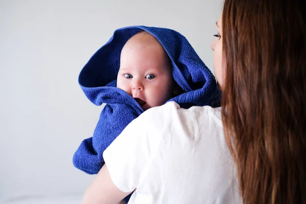 Mamãe abraça seu bebezinho mais fofo depois do banho com toalha azul na cabeça. Criança infantil em mãos de mãe. Amor maternal. Vida familiar. Mãe e bebé. Mãe feliz — Fotografia de Stock