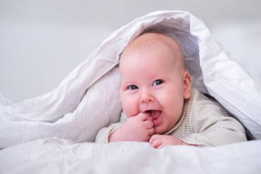 Yatak odasında beyaz battaniyenin altında gülümseyen sevimli bir oğlan. Yeni doğmuş çocuk yatakta dinleniyor. Aile sabahı evde. Yeni doğmuş bebekler.
