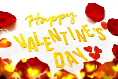 Sevgililer Günü 'nüz kutlu olsun. Kırmızı gül yaprakları ve beyaz tahta arka planda parlak kalpler olan altın yazılı tebrik kartı. romantik ve aşk konsepti