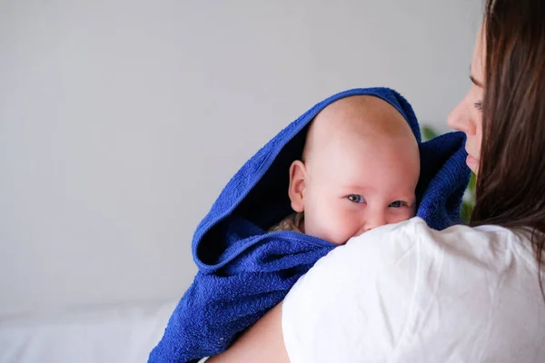 Mamãe abraça seu bebezinho mais fofo depois do banho com toalha azul na cabeça. Criança infantil em mãos de mãe. Amor maternal. Vida familiar. Mãe e bebé. Mãe feliz — Fotografia de Stock