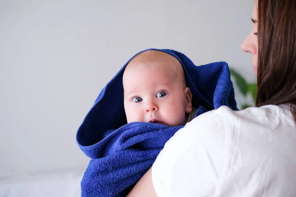 Mamãe abraça seu bebezinho mais fofo depois do banho com toalha azul na cabeça. Criança infantil em mãos de mãe. Amor maternal. Vida familiar. Mãe e bebé. Mãe feliz — Fotografia de Stock