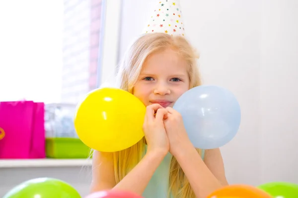 Retrato de chica rubia caucásica sonriendo en la fiesta de cumpleaños de la cámara. Fondo colorido festivo con globos. Foto vertical —  Fotos de Stock