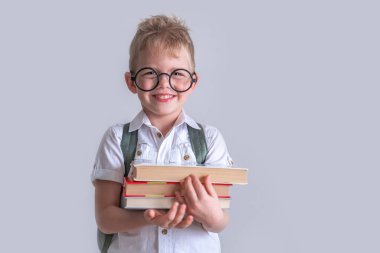 Okula dönelim. Kitapları ve beyaz gömlekli çantasıyla komik, zeki, sarışın bir ilkokul çocuğu. Eğitim. Kameraya bakıp gülümsüyor. Kopyalama alanı