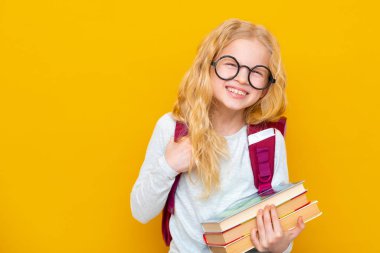 Okula dönelim. Çantalı ve kitaplı yuvarlak gözlüklü sarışın kız portresi. Sarı stüdyo geçmişi. Eğitim. Kameraya gülümsüyor. Kopyalama alanı