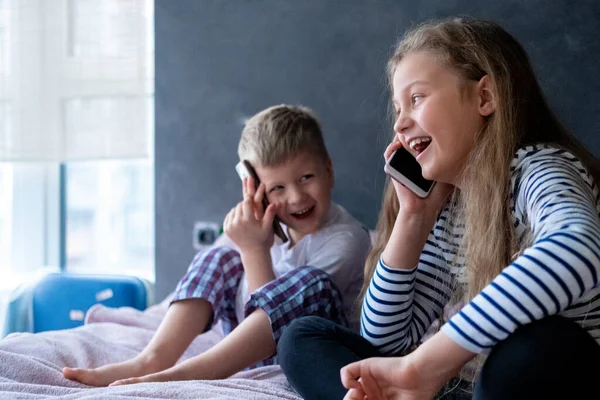 Chłopak i dziewczynka rozmawiają przez telefon komórkowy w domu. Komunikacja na odległość, połączenie, technika telefoniczna, Nowoczesne dzieciństwo — Zdjęcie stockowe