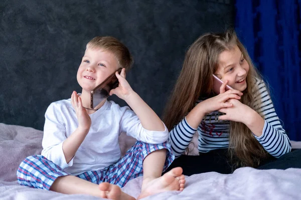 Niños exsitados chico y chica caucásicos hablan en los teléfonos móviles en casa. Comunicación a larga distancia, llamada, tecnología telefónica, infancia moderna — Foto de Stock