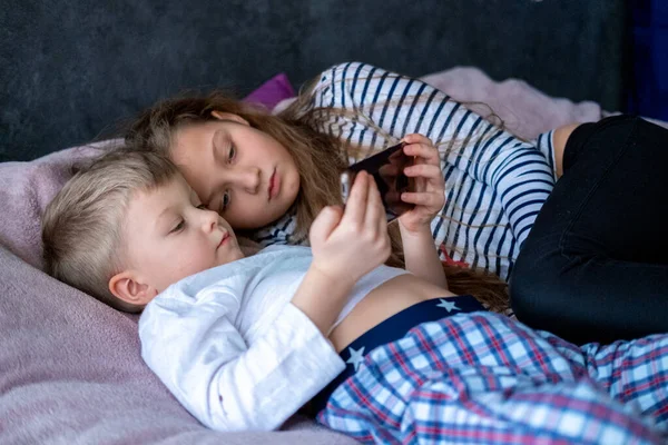 Dwójka dzieci biały chłopiec i dziewczyna grają w gry lub szuka informacji wideo tekst w Internecie na telefony komórkowe w domu leżącego w łóżku. Technologia cyfrowa, Nowoczesne dzieciństwo — Zdjęcie stockowe
