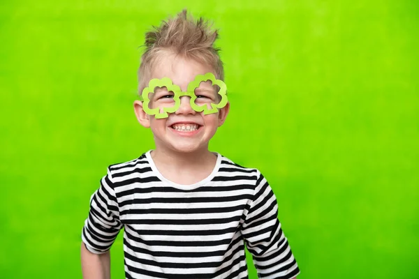 Retrato pouco sorridente caucasiano menino na máscara de leprechaun trevo copos de trevo para irlandês St. Patricks Dia no fundo do estúdio verde. Espaço de cópia — Fotografia de Stock