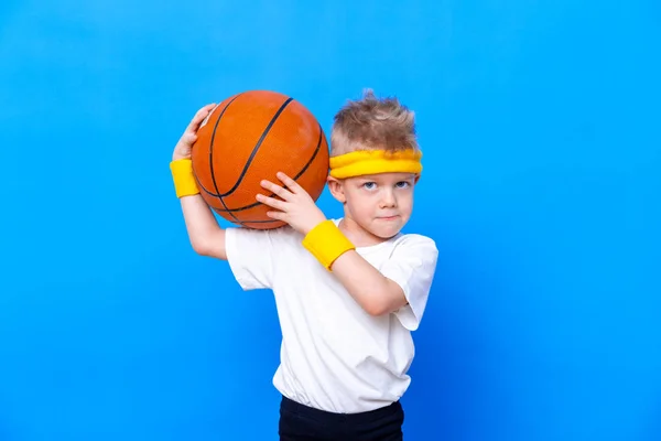 Sportief jongetje met basketbal over blauwe studioachtergrond. Gym training. Kindersportman. Activiteit. Sport. Fitness, gezondheid en energie. Succes — Stockfoto