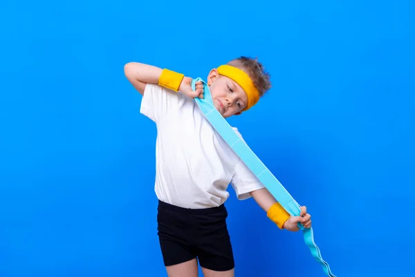 Sportief jongetje met rubberen fitnessband over blauwe studioachtergrond. Gym training. Kindersportman. Activiteit. Sport, gezondheid en energie. Succes — Stockfoto