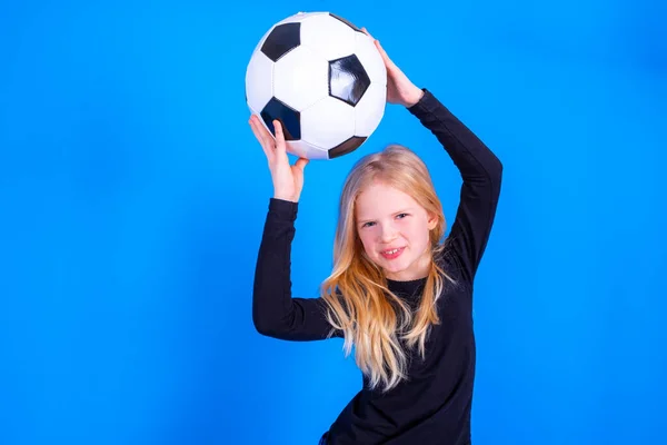 Fanoušci fotbalu. Roztomilé blondýny dívka v černé košili zvedl míč nad hlavu na modrém pozadí studia. Kopírovací prostor. Fotbalový zápas. — Stock fotografie