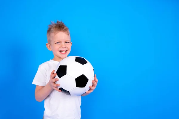 Voetbalfans. Glimlachende blanke jongen die voetbal in handen houdt over een blauwe studio achtergrond. Kopieerruimte. Voetbalwedstrijd. — Stockfoto