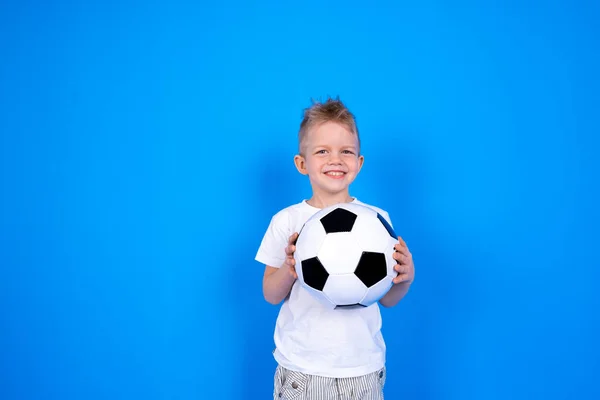 Voetbalfans. Glimlachende blanke jongen die voetbal in handen houdt over een blauwe studio achtergrond. Kopieerruimte. Voetbalwedstrijd. — Stockfoto