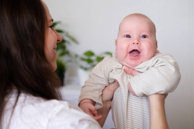 Mutlu bebek. Küçük sevimli tombul beyaz beyaz bebek anne ellerinde kameraya bakıp gülümsüyor. Aile hayatı, anneler sevgisi, annelik.