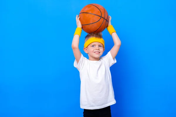 Σπορ αγοράκι με μπάλα μπάσκετ πάνω από μπλε φόντο στούντιο. Γυμναστική γυμναστική. Παιδικός αθλητής. Δραστηριότητα. Αθλητισμός. Γυμναστική, υγεία και ενέργεια. Επιτυχία — Φωτογραφία Αρχείου