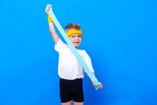 Menino desportivo com faixa de borracha fitness sobre fundo estúdio azul. Treino de ginástica. Desportista infantil. Actividade. Desporto, saúde e energia. Sucesso — Fotografia de Stock