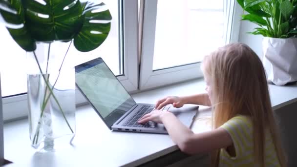 Маленька блондинка працює, вчиться або грає на ноутбуці. натисніть палець на кнопки. Цифрова освіта. Комп'ютерні технології, соціальні медіа та Інтернет. 4k кадрів — стокове відео