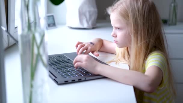 Niña rubia trabajando, estudiando o jugando en un ordenador portátil. presiona los botones con el dedo. Educación digital. Tecnología informática, redes sociales e Internet. Imágenes de 4k — Vídeo de stock