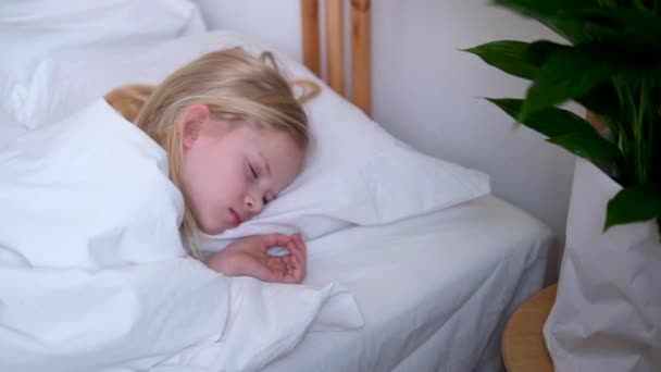 Menina loira dormindo em cama grande com roupa de cama branca no início da manhã. Vista superior. As crianças sonham. Infância, calma, noite .4k filmagem . — Vídeo de Stock