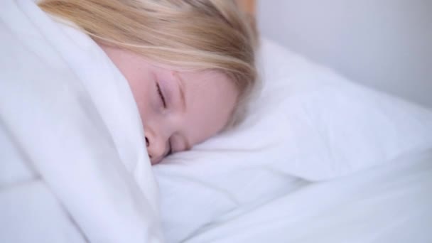 Sabahın erken saatlerinde büyük bir yatakta beyaz çarşafla uyuyan küçük sarışın kız. Çocuklar rüya görür. Çocukluk, sakinlik, gece çekimleri.. — Stok video
