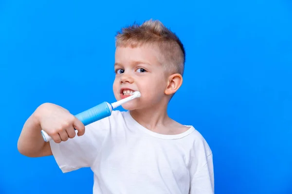 Niño niño feliz niño cepillarse los dientes con cepillo de dientes eléctrico sobre fondo azul. Salud, higiene dental. Mockup, espacio de copia. — Foto de Stock