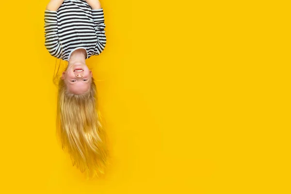 Opgewonden kleine blonde meisje opknoping gelukkig ondersteboven over geïsoleerde gele studio achtergrond. Emotie, expressie. Kopieer ruimte voor tekst — Stockfoto
