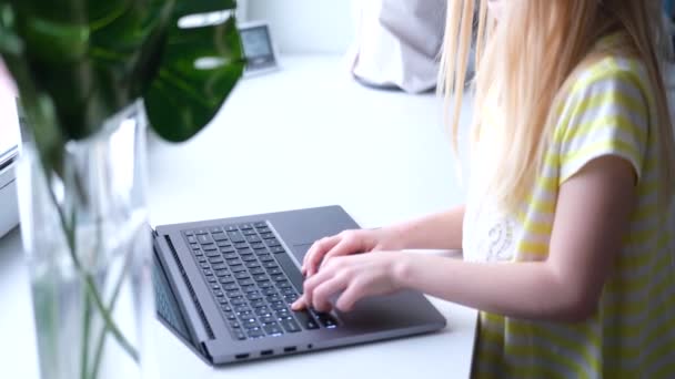 Маленькая блондинка работает, учится или играет на ноутбуке. нажми на кнопки. Цифровое образование. Компьютерные технологии, социальные сети и Интернет. 4k кадров — стоковое видео