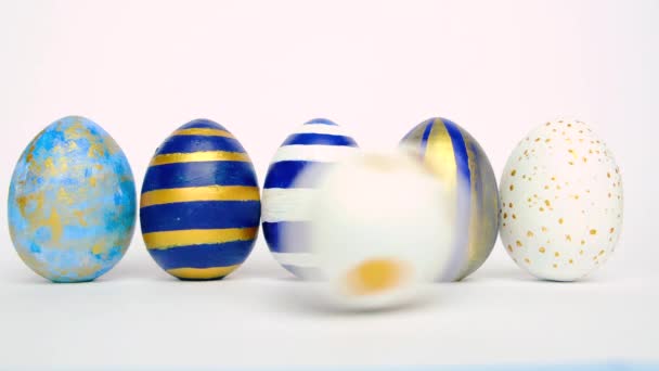 Le uova di Pasqua stanno rotolando, bussando a vicenda sul tavolo bianco. Uova trendy colorate classiche blu, bianche e dorate. Buona Pasqua. Stile minimale . — Video Stock