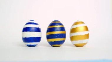 Paskalya yumurtaları yuvarlanıyor, birbirlerini beyaz masaya vuruyorlar. Yumurtaların modası geçmiş klasik mavi, beyaz ve altın rengi. Mutlu Paskalyalar. Asgari biçim. 