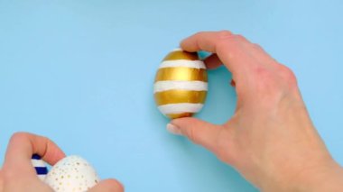 Dişi eller mavi bir masanın üzerine beş tane paskalya yumurtası bırakır. Yumurtaların modası geçmiş klasik mavi, beyaz ve altın rengi. Mutlu Paskalyalar. Asgari düzeyde. Üst görünüm