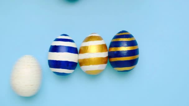 Easter eggs are rolling, knocking each other on blue table. Eggs trendy colored classic blue, white and golden . Happy Easter. Minimal style. Top view