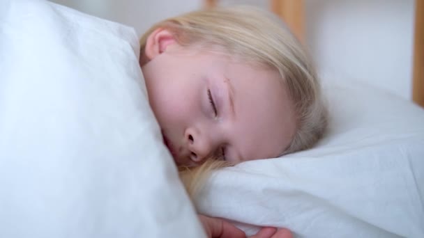 Dormir niña rubia de cerca en la cama grande con ropa de cama blanca temprano en la mañana. Niños sueñan. Infancia, calma, noche .4k metraje . — Vídeos de Stock