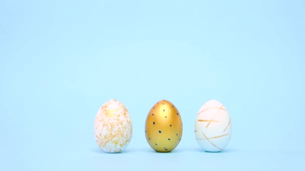 Пасхальные яйца катятся, стуча друг друга по синему столу. Яйца модного цвета классический синий, белый и золотой. Счастливой Пасхи. Минимальный стиль. — стоковое видео