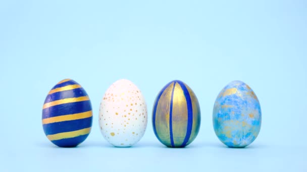 Пасхальні яйця котяться, стукають один одного на синьому столі. Яйця модно забарвлені класичним синім, білим і золотим. З Великоднем. Мінімальний стиль. — стокове відео