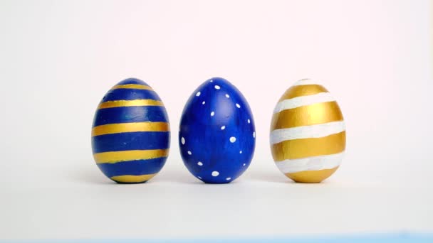 Los huevos de Pascua están rodando, golpeándose unos a otros en la mesa blanca. Huevos de moda de color clásico azul, blanco y dorado. Feliz Pascua. Estilo mínimo . — Vídeo de stock