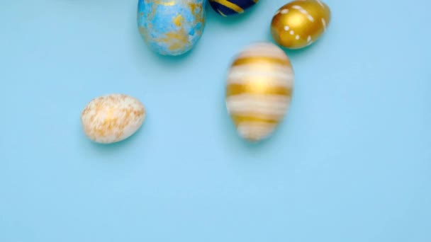 Easter eggs are rolling, knocking each other on blue table. Eggs trendy colored classic blue, white and golden . Happy Easter. Minimal style. Top view — Stock Video