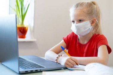 Distance learning online education. Sickness schoolgirl in medical mask studying at home, looking at laptop notebook and doing school homework. Training books and notebooks on table. clipart
