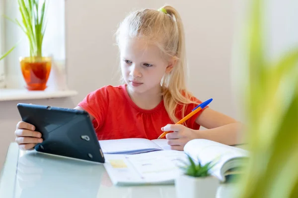 Enseignement à distance en ligne. Écolière étudiant à la maison avec tablette numérique et faisant des devoirs scolaires. Livres de formation et cahiers sur table . — Photo