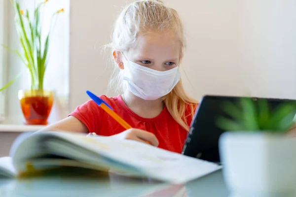 Uzaktan öğrenme çevrimiçi eğitim. Tıp maskeli hasta kız elinde dijital tabletle evde ders çalışıyor ve ödev yapıyor. Coronavirüs karantinası