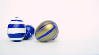 Paskalya yumurtaları yuvarlanıyor, birbirlerini beyaz masaya vuruyorlar. Yumurtaların modası geçmiş klasik mavi, beyaz ve altın rengi. Mutlu Paskalyalar. Asgari biçim. 