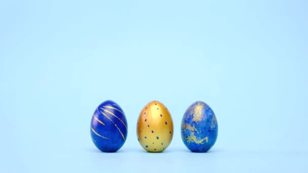 Easter eggs are rolling, knocking each other on blue table. Eggs trendy colored classic blue, white and golden . Happy Easter. Minimal style. — Stock Video