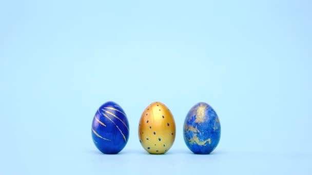 A húsvéti tojások gurulnak, egymást verik a kék asztalon. Tojás trendi színű klasszikus kék, fehér és arany. Boldog Húsvétot! Minimális stílus. 