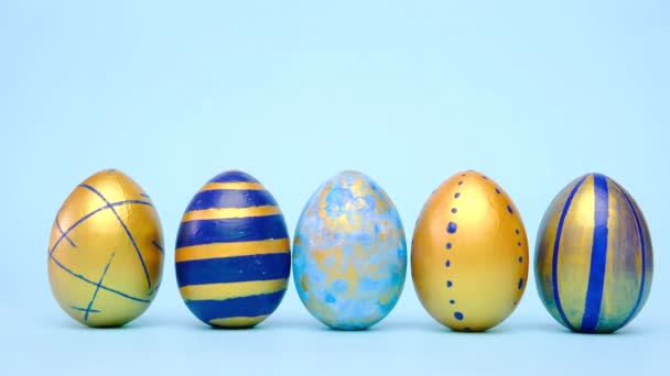 Los huevos de Pascua están rodando, golpeándose unos a otros en la mesa azul. Huevos de moda de color clásico azul, blanco y dorado. Feliz Pascua. Estilo mínimo. — Vídeo de stock