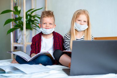 Uzaktan öğrenme çevrimiçi eğitim. Hasta okul çocuğu ve maskeli kız evde dijital tablet dizüstü bilgisayarla ders çalışıyor ve ödev yapıyor. Eğitim kitaplarıyla yatakta oturmak.