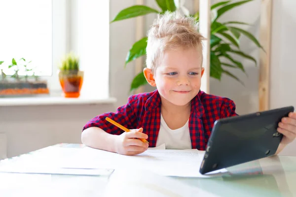 Kształcenie online na odległość. Uczeń uczy się w domu z tabletem cyfrowym i odrabia lekcje. Książki szkoleniowe i zeszyty na stole. — Zdjęcie stockowe